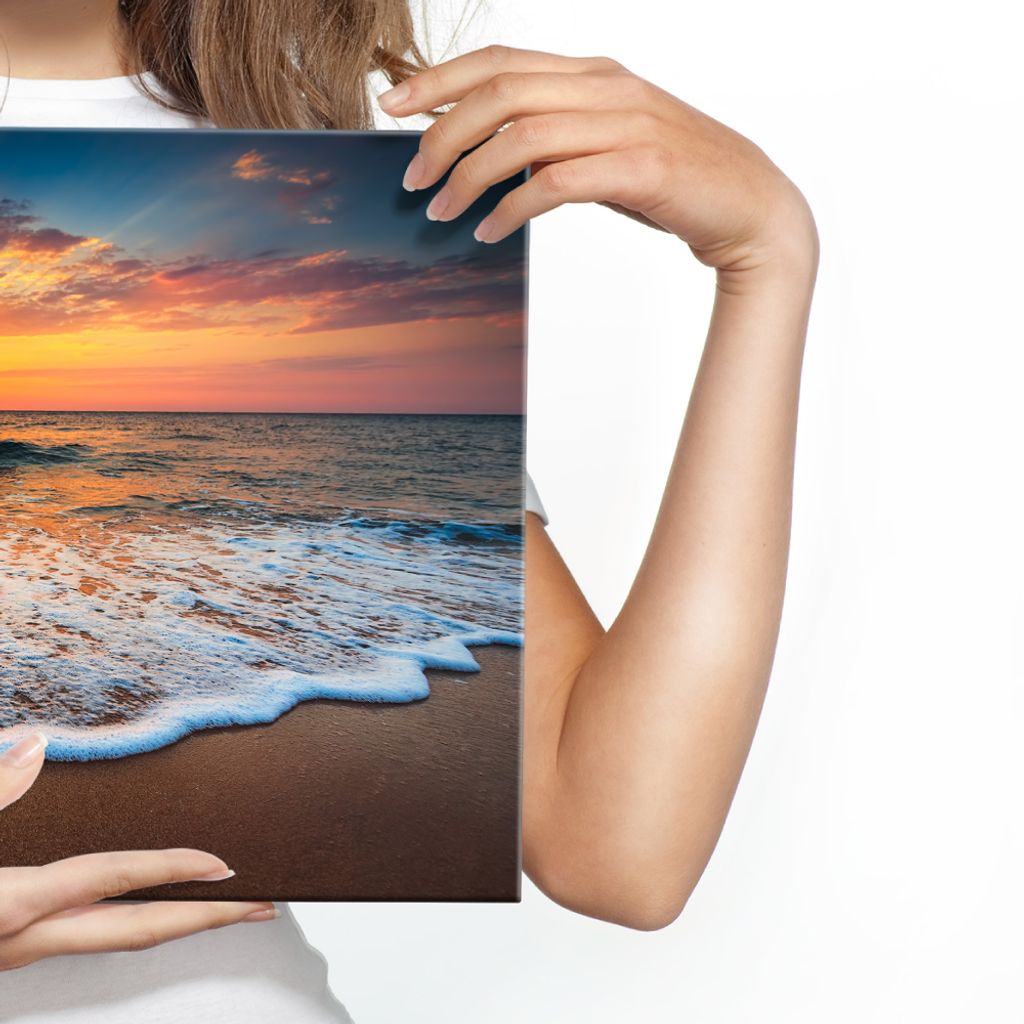 A person is holding a canvas print of a beach sunset.