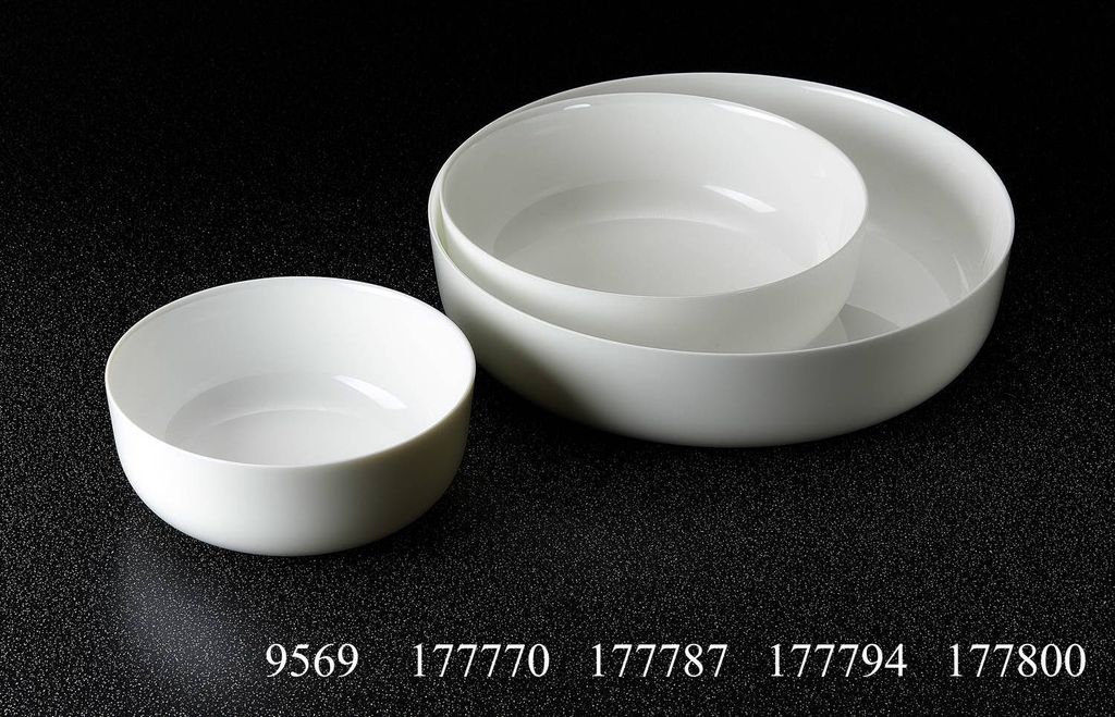 Three white ceramic bowls are arranged on a black surface. One small bowl is in the foreground to the left, and two larger bowls are nested together in the background to the right.