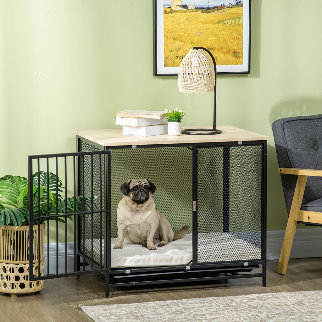 A pug sits inside a dog crate that doubles as a side table, with a lamp and books on top.