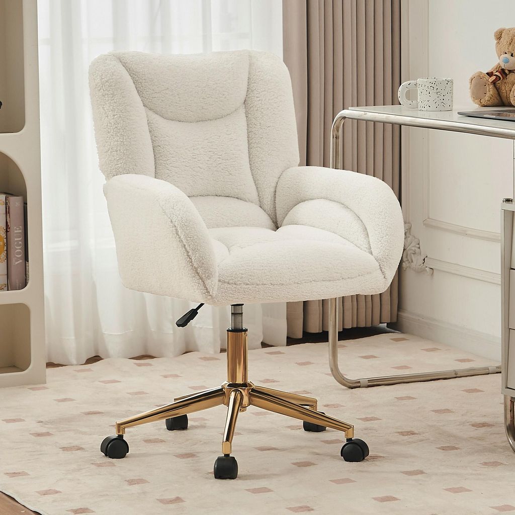 A fluffy white office chair with gold legs sits on a patterned rug in a room with sheer curtains and a desk.