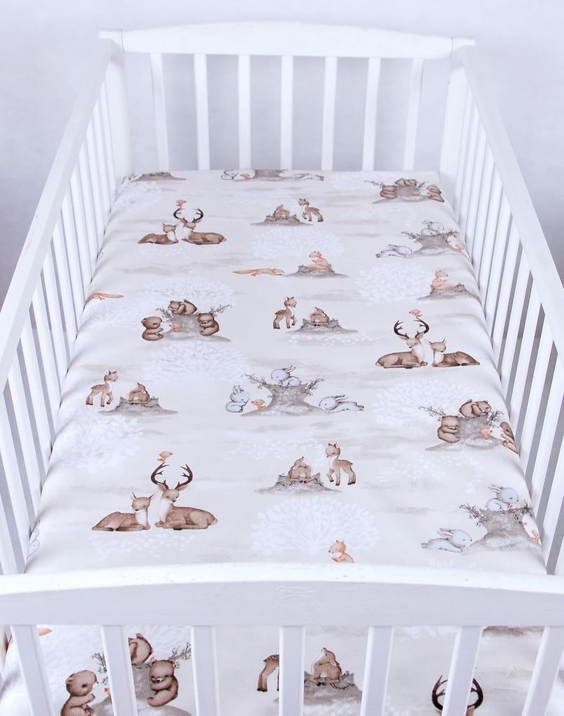 A crib sheet with a woodland animal pattern is laid out flat inside a white crib.