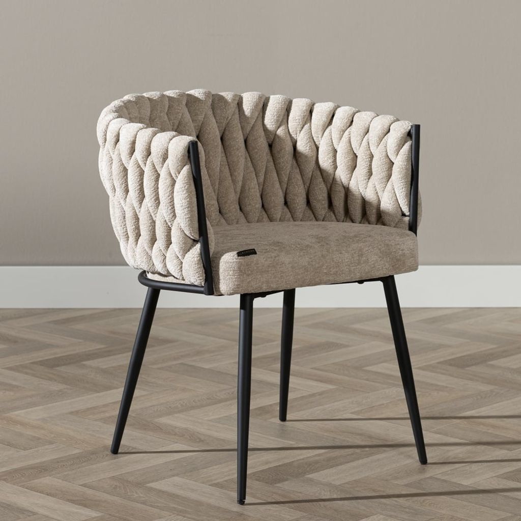 A beige upholstered chair with black metal legs is shown against a light gray wall and a wooden floor.