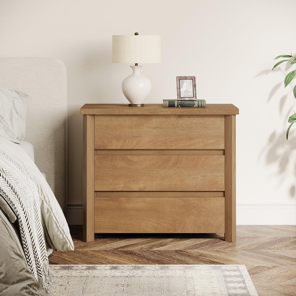 A bedside table with a lamp and a framed picture on top, next to a bed.
