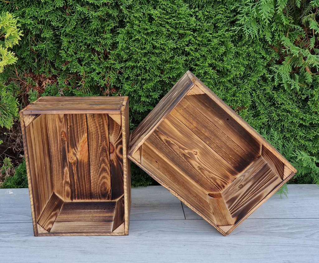 Two wooden crates are placed on a gray surface in front of a green hedge.