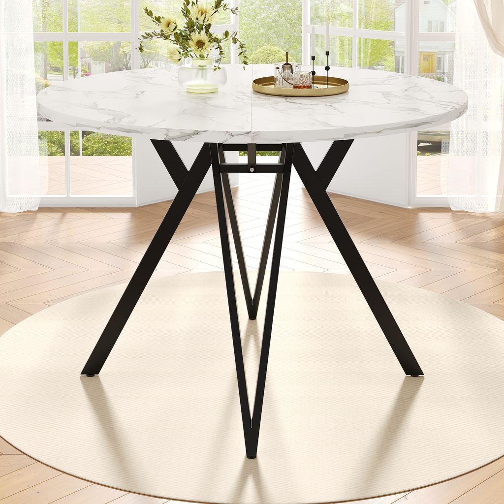 A round dining table with a marble-like top and black metal legs, set in a bright room with large windows.