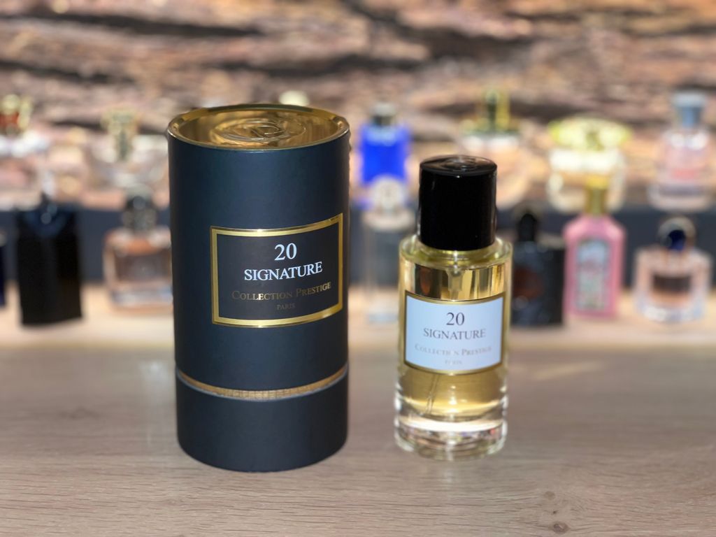 A perfume bottle and its cylindrical packaging are displayed on a wooden surface, with other perfume bottles blurred in the background.