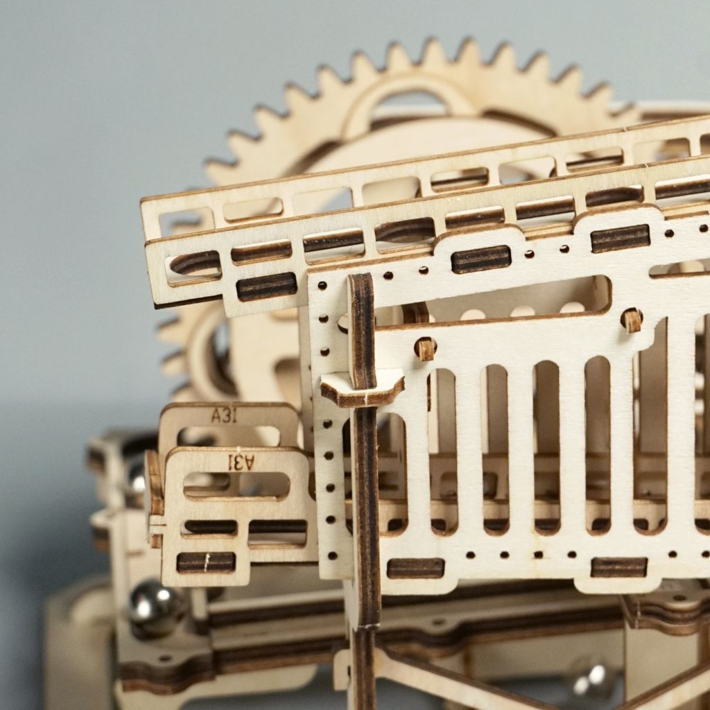 A close-up view of a wooden mechanical model kit, likely a marble run or robot.