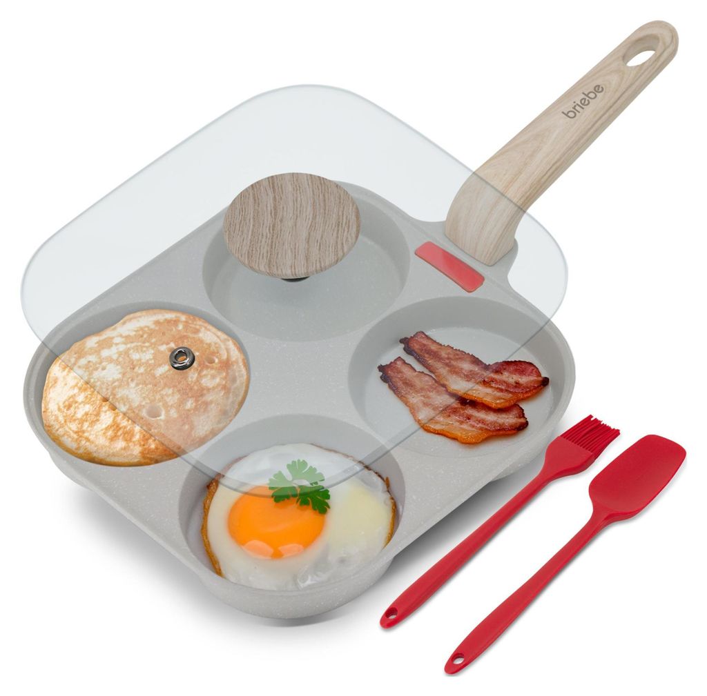 A multi-compartment frying pan with a glass lid, containing a pancake, bacon, and a fried egg. Also includes red silicone cooking utensils.