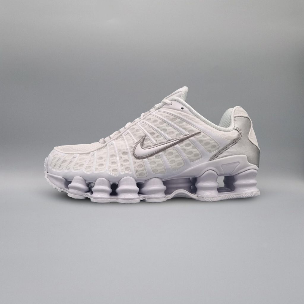 A white Nike Shox TL sneaker with silver accents is shown against a light gray background.
