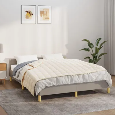 A bed with a cream-colored weighted blanket and pillows in a bedroom setting.