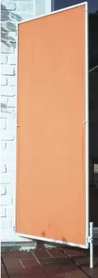An orange privacy screen or partition standing on a tiled floor against a brick wall.