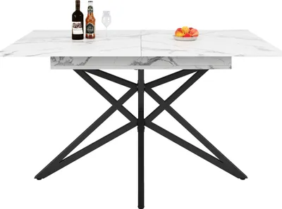 A white marble-patterned dining table with a black metal base, set against a white background. Two bottles of wine and a glass are on the table, along with a small bowl of fruit.