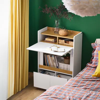 A compact desk with shelves and drawers, set up in a bedroom next to a yellow curtain and a bed with plaid bedding.