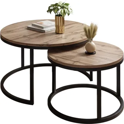 A set of two round nesting coffee tables with a wood-look top and black metal legs, decorated with a plant and a small vase.