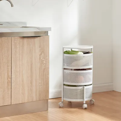 A white, three-tiered rolling storage cart filled with produce is shown next to a kitchen counter.