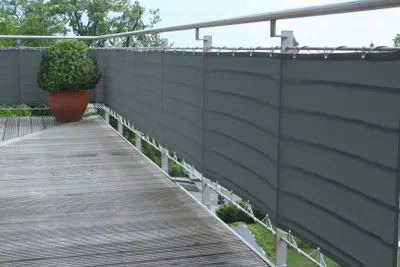 A balcony with a wooden floor and a gray privacy screen attached to the railing. A potted plant is visible on the left.
