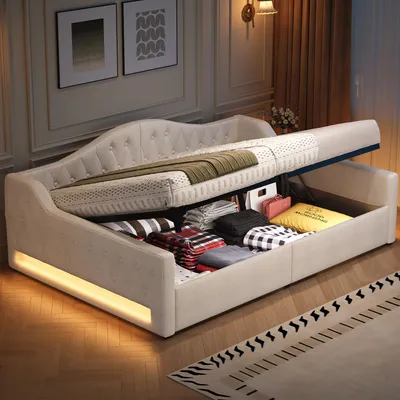 A beige daybed with its mattress lifted to reveal storage space filled with folded linens and pillows. The bed has LED lighting along its base.