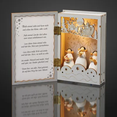 An open decorative wooden book with a Christmas scene inside, featuring angels and a sleigh. The left page has a poem written on it.