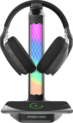 A black headphone stand with RGB lighting, holding a pair of black headphones, and a smartphone charging on its base.