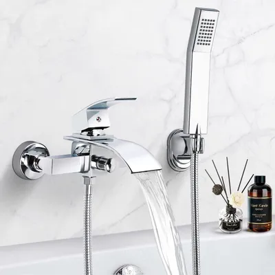 A modern chrome bathtub faucet with a waterfall spout and a handheld showerhead is shown against a marble-tiled wall.