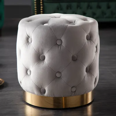A close-up shot of a tufted ottoman with a gold base.