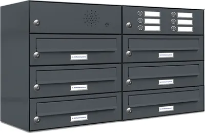 A dark gray, multi-unit mailbox system with individual compartments, each featuring a lock and a label slot. The top section includes a speaker grille and buttons with label areas.