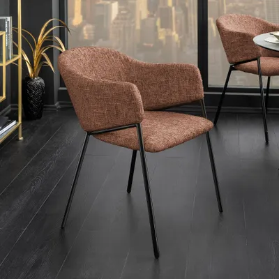 A brown upholstered chair with a black metal frame is shown in a room with a dark wooden floor and a large window overlooking a cityscape.