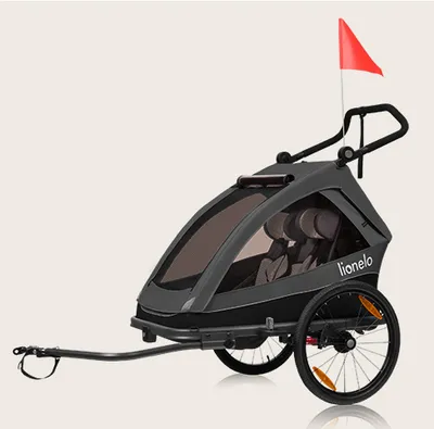 A gray and black child trailer for bicycles or as a stroller, with a red flag on top.