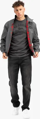 A man is standing and posing for a product shot, wearing a jacket, t-shirt, and jeans.
