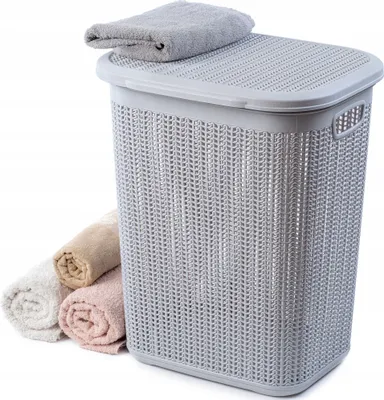 A laundry basket with a lid and rolled towels next to it, on a white background.