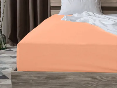 A close-up view of a peach-colored fitted sheet on a bed.