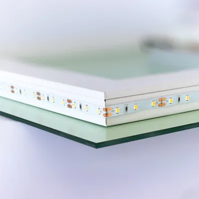 A close-up shot of the edge of a rectangular mirror with LED lights attached to its frame, resting on a glass surface.