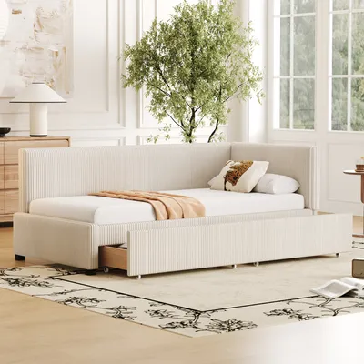 A beige upholstered daybed with drawers is shown in a well-lit room with large windows and a tree visible outside.