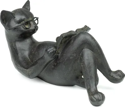 A dark gray statue of a cat wearing glasses and reading a book, lying on its back.