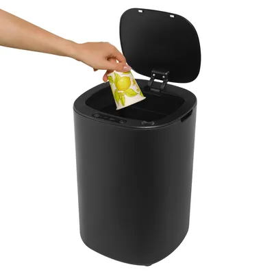 A hand is shown placing a paper cup with a lemon design into a black smart sensor trash can.