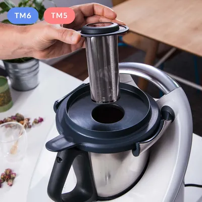 A hand is shown inserting a stainless steel tea strainer into a kitchen appliance.
