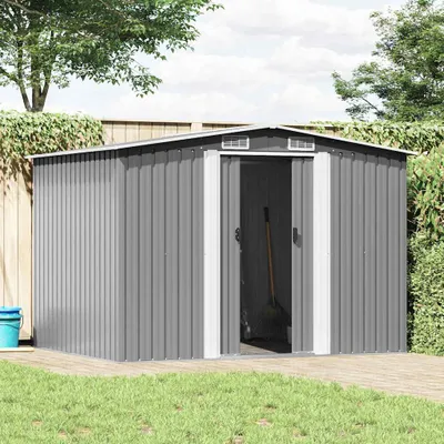 A grey metal garden shed is shown in a backyard setting with grass and a wooden deck.