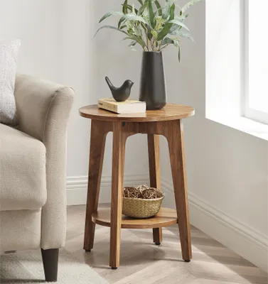 A round wooden side table with a vase of greenery, a decorative bird, and a small basket on it, placed next to a sofa.