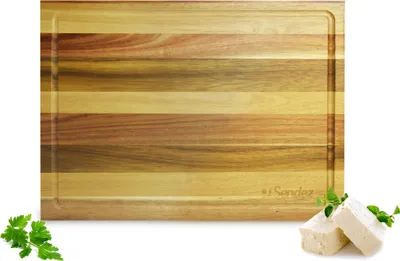 A wooden cutting board with a juice groove, shown on a white background with some parsley and cheese cubes.