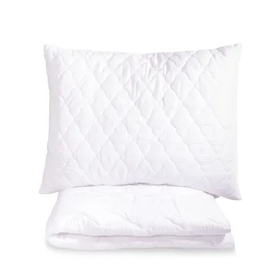 A white quilted pillow and a folded white quilted blanket are stacked on a white background.