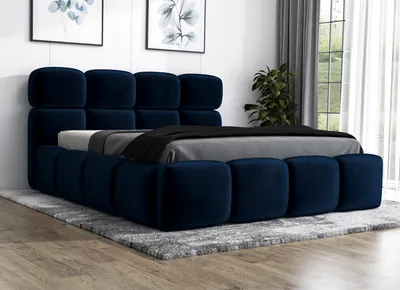 A modern upholstered bed with a plush navy blue velvet finish, set in a bedroom with artwork on the wall and a large window with curtains in the background.