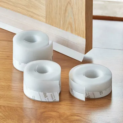 Three rolls of white sealing tape are placed on a wooden floor in front of a wooden door frame.