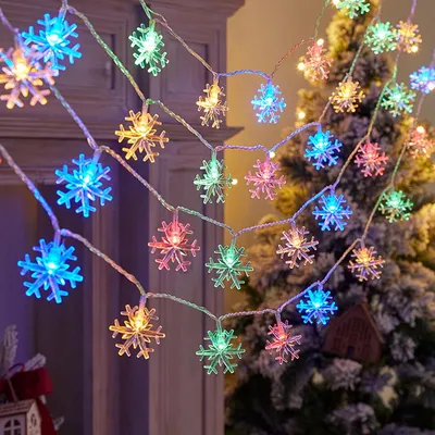 A string of snowflake-shaped LED lights is draped around a Christmas tree and a fireplace.