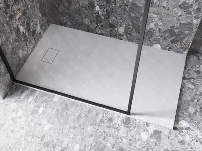 A close-up view of a modern shower tray with a stone effect finish, set within a bathroom with marble-effect tiles.