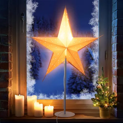 A festive Christmas scene on a windowsill, featuring a large illuminated star lamp, candles, and a small decorated Christmas tree.