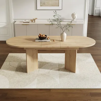 A light wood dining table with a modern design, set on a patterned rug in a well-lit room with a sideboard in the background.