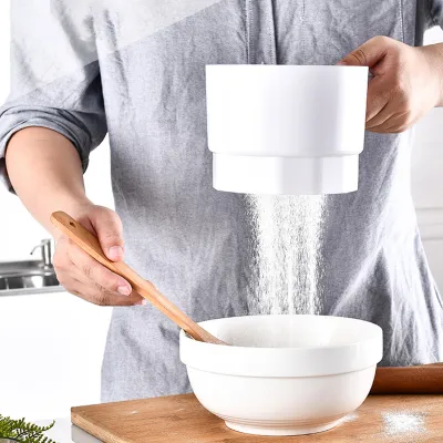 A person is sifting flour into a bowl using a flour sifter.