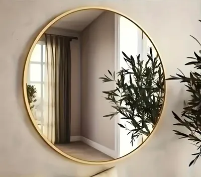 A round mirror with a gold frame hangs on a wall, reflecting a room with curtains and a plant.