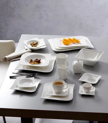 A collection of white ceramic tableware, including plates, bowls, cups, and a creamer, arranged on a table.