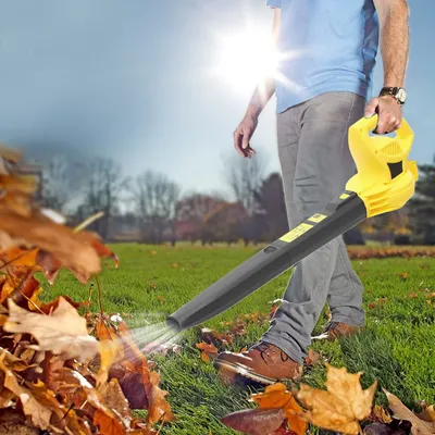 A person is using a yellow and black leaf blower to clear fallen leaves from a grassy lawn on a sunny day.